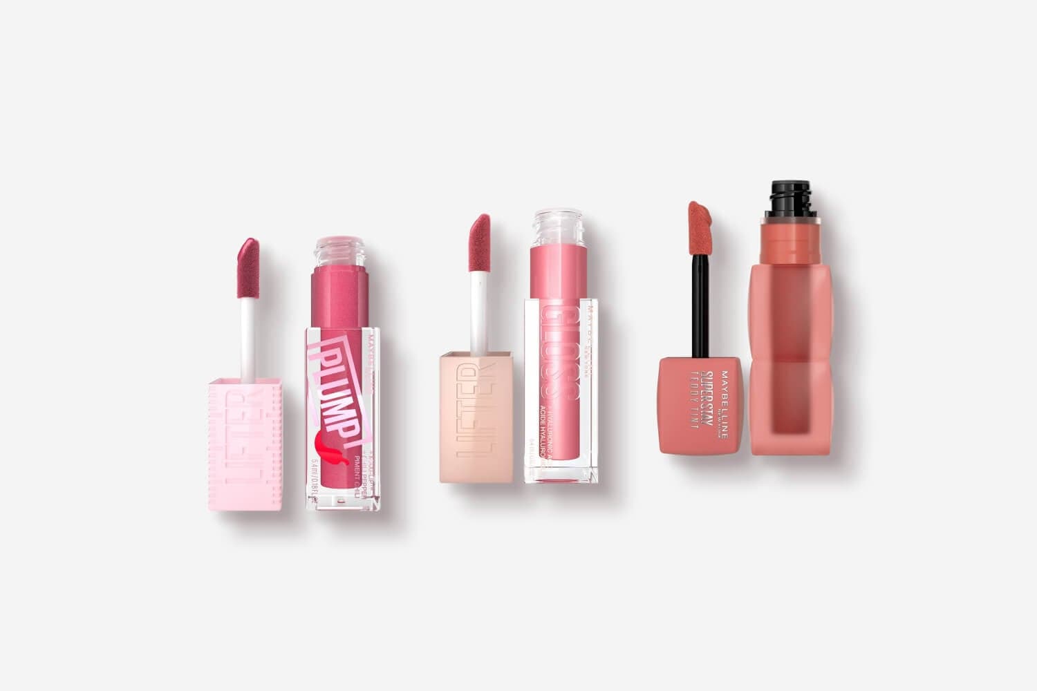 Three open Maybelline lip products on grey: Lifter Plump in berry pink, Lifter Gloss in soft pink and SuperStay Teddy Tint in nude.