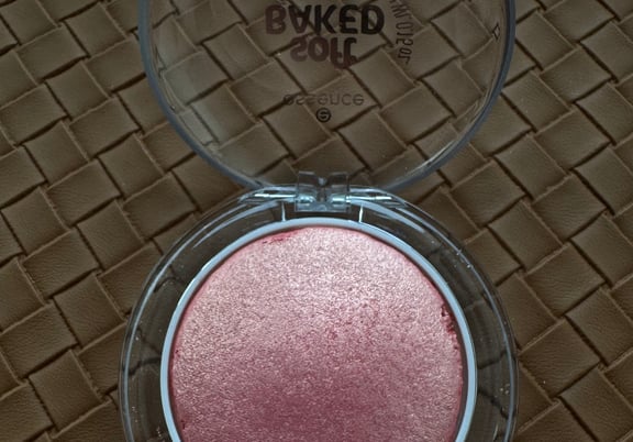 Pink shimmery baked blush in a round clear plastic compact on a woven brown surface. review
