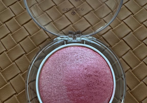 Round compact with clear lid showing a shimmery pink baked powder blush inside. review