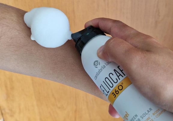 A foamy sunscreen mousse is being dispensed onto an arm from a white and yellow canister. review