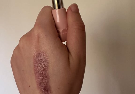 A hand holding a lipstick with a pink tube, showing a shimmery mauve swatch on the skin. review